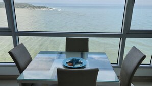 Un tavolo da pranzo con sedie e vista sul mare attraverso ampie finestre.