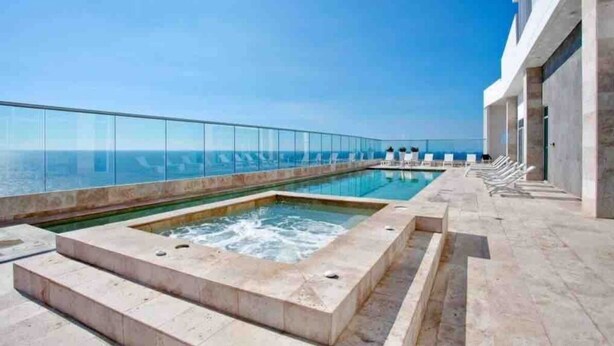 Una piscina sul tetto con ringhiera in vetro, una vasca idromassaggio e lettini da relax.