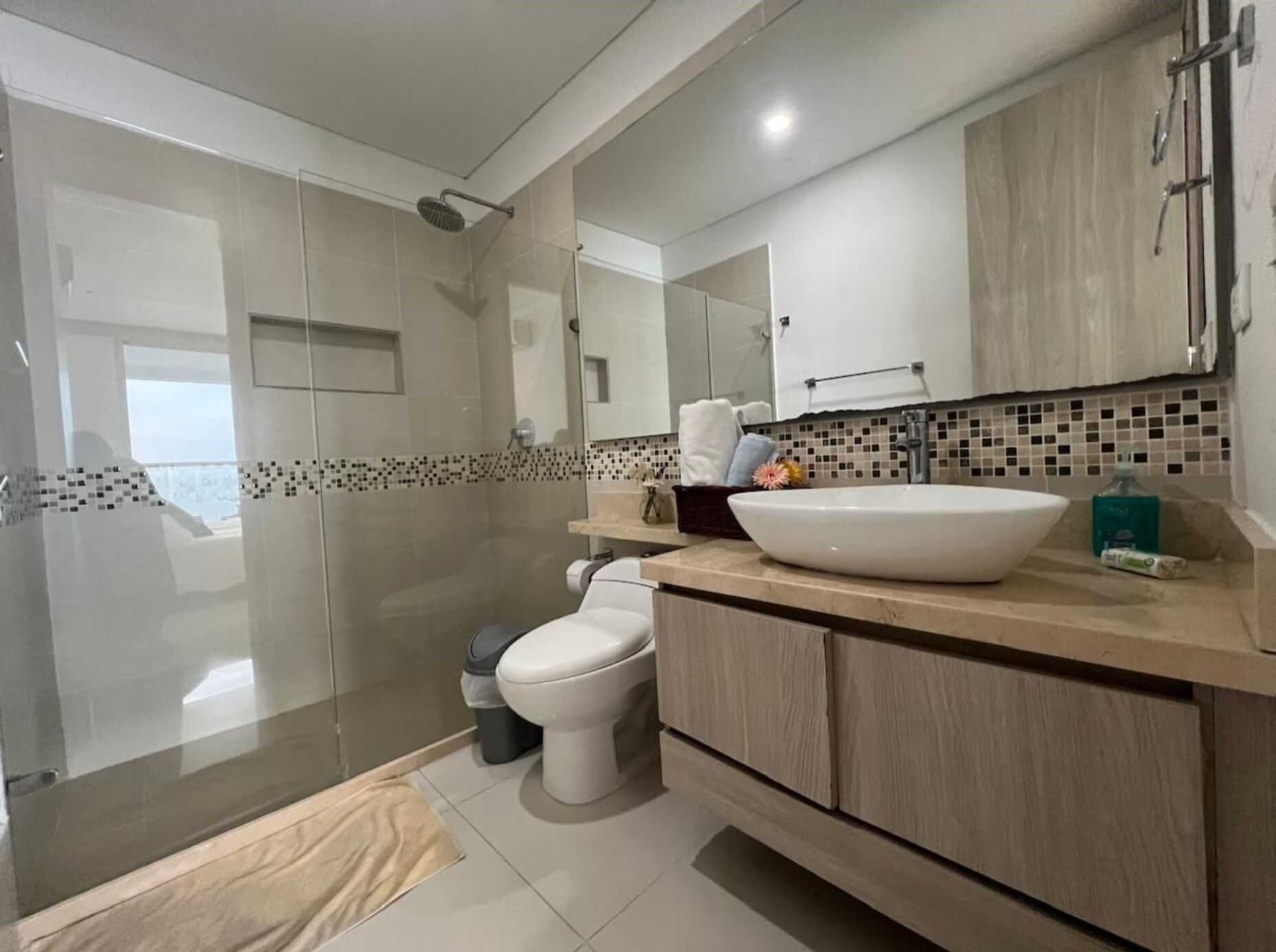 A modern bathroom with a glass-enclosed shower, a white toilet, and a large vanity with a vessel sink.