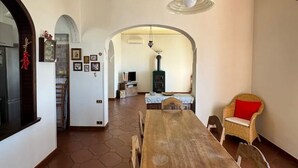 Un coin repas avec une table et des chaises en bois, un luminaire suspendu et une vue sur une autre pièce dotée d’une cheminée.