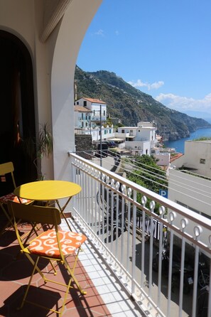 Un balcon avec des chaises jaunes et une table, donnant sur une ville côtière avec ses bâtiments et une montagne.