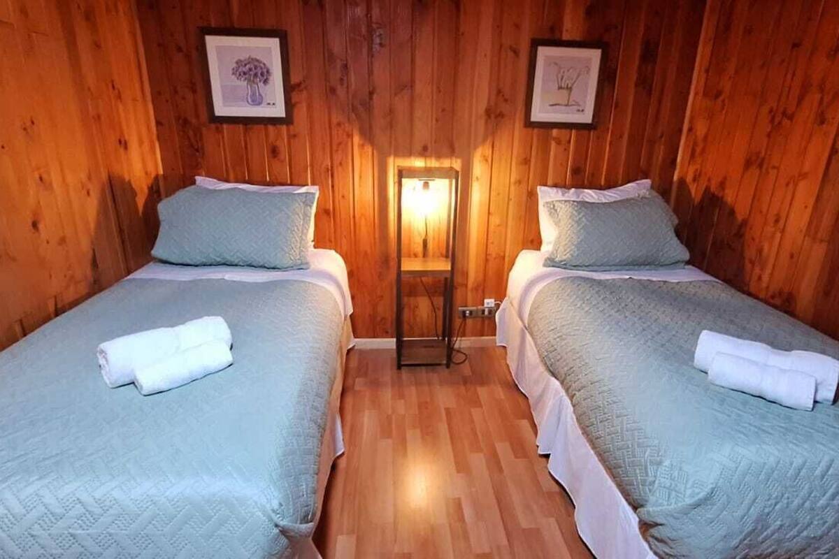 Quarto com duas camas, paredes de madeira, uma mesa pequena e um quadro na parede.