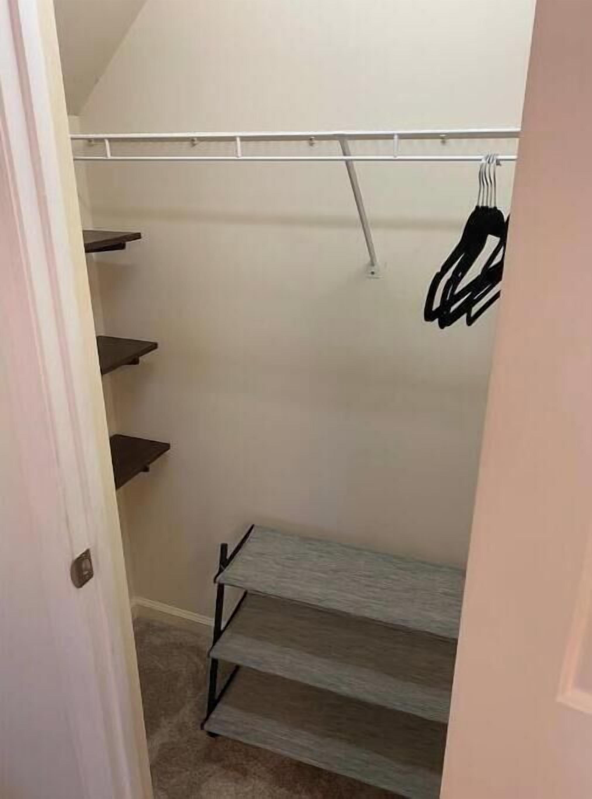 A walk-in closet with a metal rod for hanging clothes, a grey shelf unit, and a door partially open.