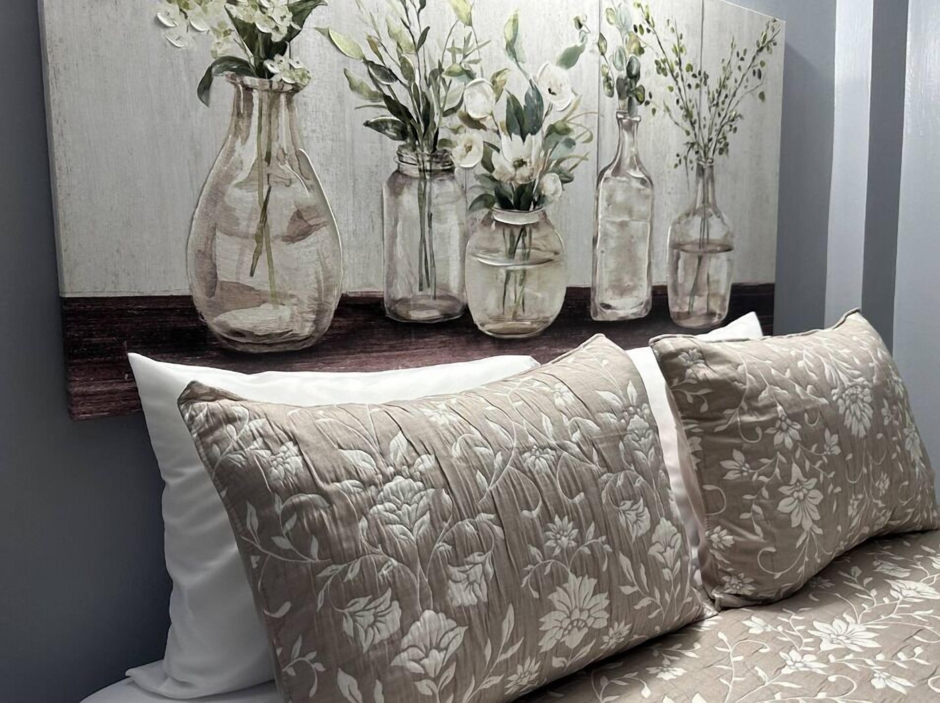 Een kamer met een bed, een schilderij met vazen en bloemen aan de muur, en een houten hoofdbord.