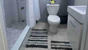 A bathroom with a shower, toilet, and sink. There are two framed pictures on the wall and a towel rack with towels.