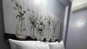 A bed with white bedding, a floral-patterned throw, and a wall with four vases of flowers.