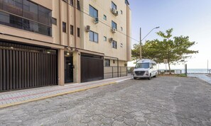 Un edificio con grandes puertas de garaje, una furgoneta estacionada y un área pavimentada con un banco y árboles.