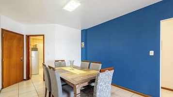 Uma área de refeições com mesa e cadeiras de madeira, uma parede azul decorativa e uma porta que dá para uma cozinha.