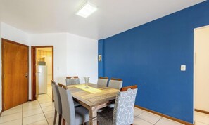 Un comedor con una mesa y sillas de madera, un muro azul decorativo y una puerta que da a una cocina.