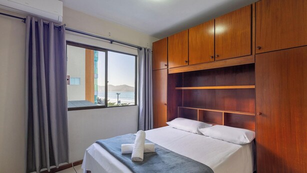 A hotel room with a bed, a window with curtains, and wooden wardrobe. - Beachfront Apartment With Beach View Vte0301 (Itapema)