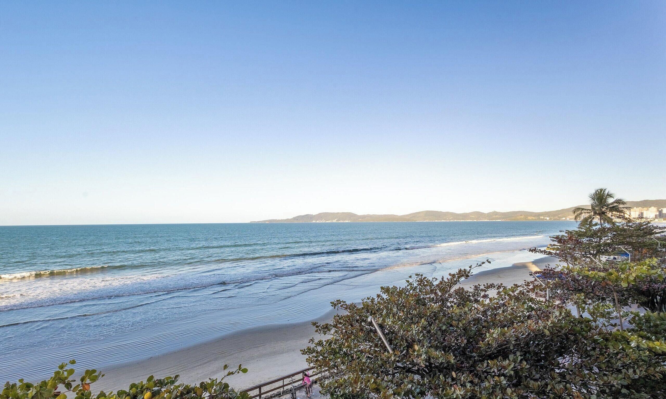 A beach with clear skies, calm water, and distant hills.