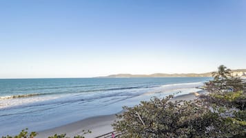 Uma praia com céu claro, águas calmas e colinas ao longe.
