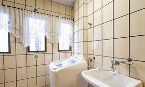 Baño con lavadora, lavamanos y dos ventanas con cortinas de encaje.