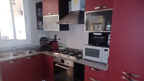 A kitchen with red cabinets, a gas stove, a microwave, and a sink.