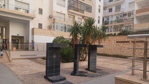 A multi-story residential building with balconies, a gated entrance, and a landscaped courtyard with steps and planters.