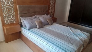 A bedroom with a wooden headboard, a bed with striped bedding, and a nightstand with a decorative panel.