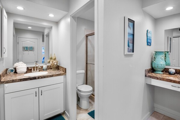 A modern bathroom with a white sink, vanity, and toilet. There are decorative items on the countertop and a large vase on the wall. - Our House at the Beach C-110: Across the street from the beach! (Siesta Key)