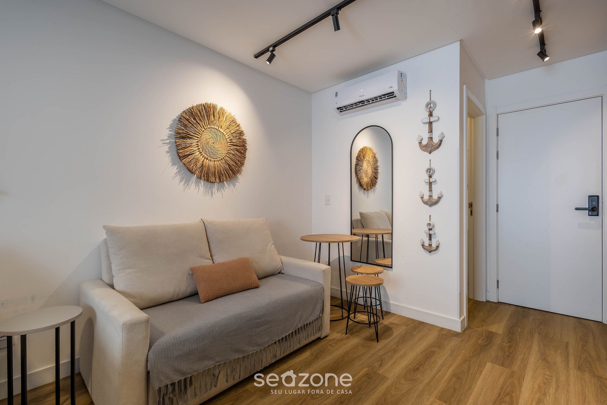 En moderne stue med sofa, rund vægdekoration, lille bord og et spejl med dekorative detaljer.