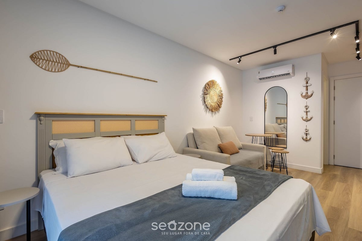 A modern hotel room with a bed, a sofa, a small table, and a mirror.