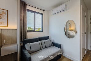 Una sala de estar moderna con sofá, un ventanal grande, un equipo de aire acondicionado y un espejo en la pared.