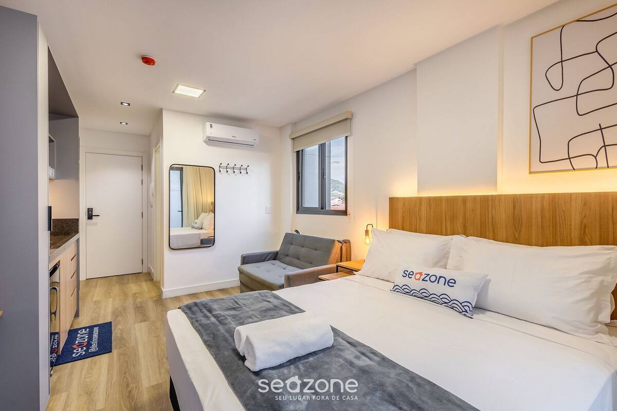 A modern hotel room with a bed, a seating area, a window, and a view of the outside.