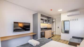 A modern hotel room with a flat-screen TV, a sofa, a dining area with a sink, and a mirror.