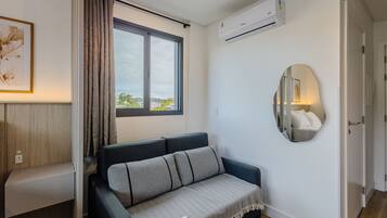 A modern living room with a sofa, a large window, an air conditioning unit, and a mirror on the wall.