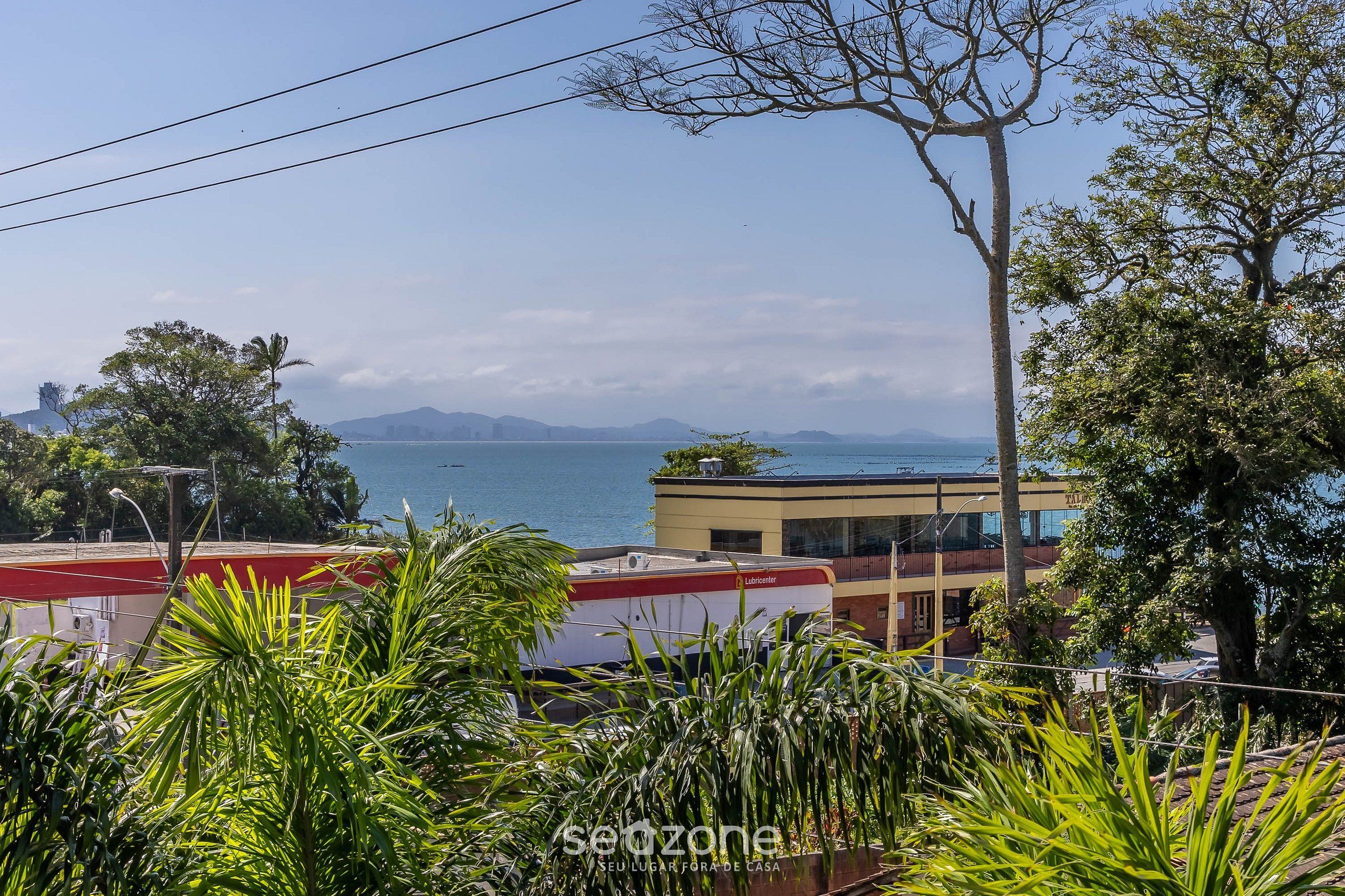 A coastal view with a building, palm trees, and a clear sky.