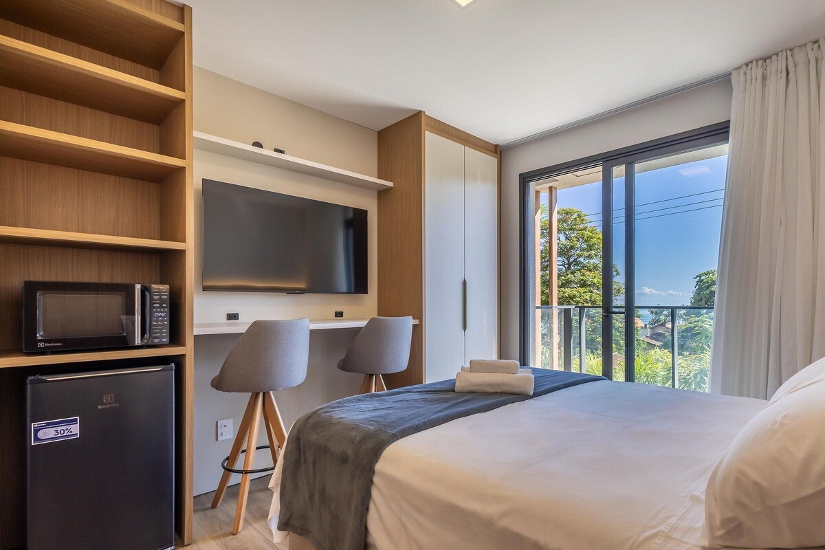 A hotel room with a bed, a desk with chairs, a TV, and a balcony with a view.