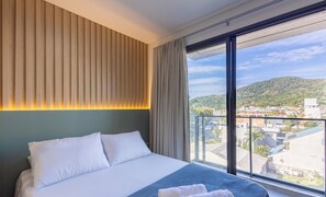 A hotel room with a large bed, a view of a cityscape, and a balcony with a mountain backdrop. - New Studios - Pool With sea View - Penha Spot PSO (Penha)
