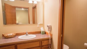 Un baño con tocador de madera, lavamanos, espejo, secador de pelo y retrete.