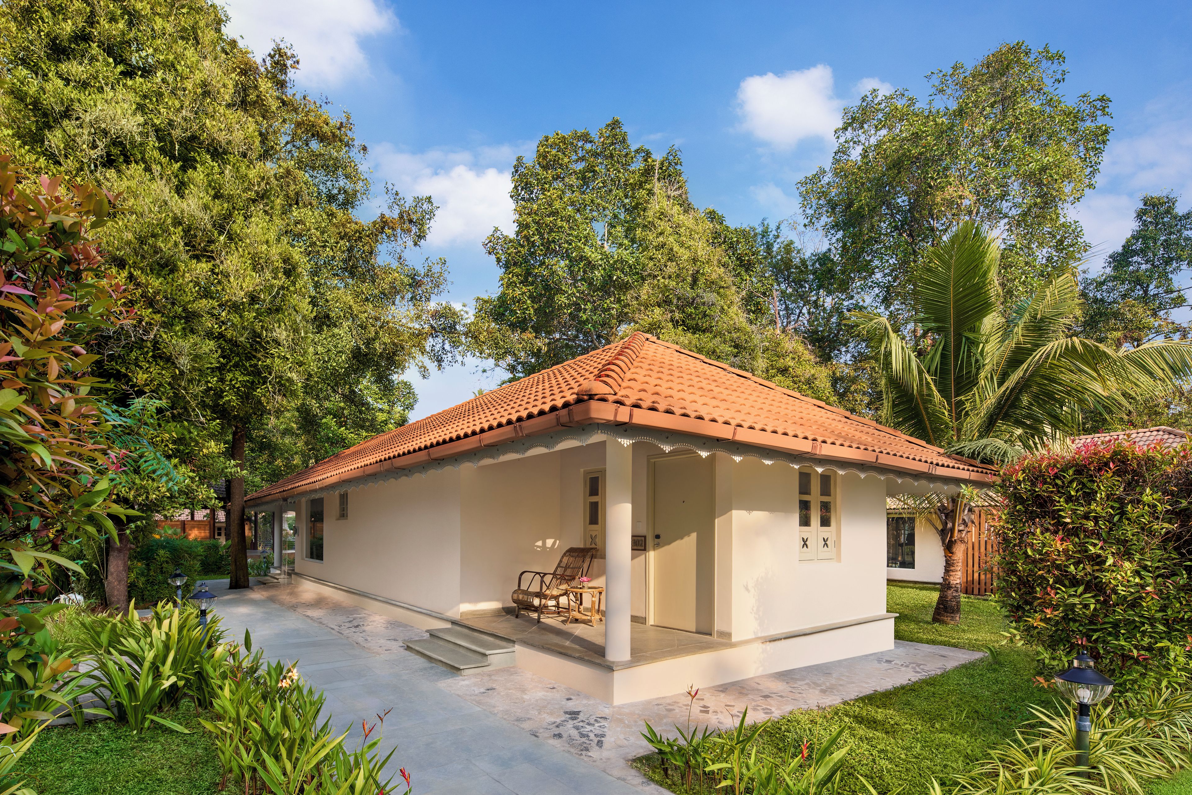 A small, single-story house with a tiled roof, surrounded by lush greenery and trees.
