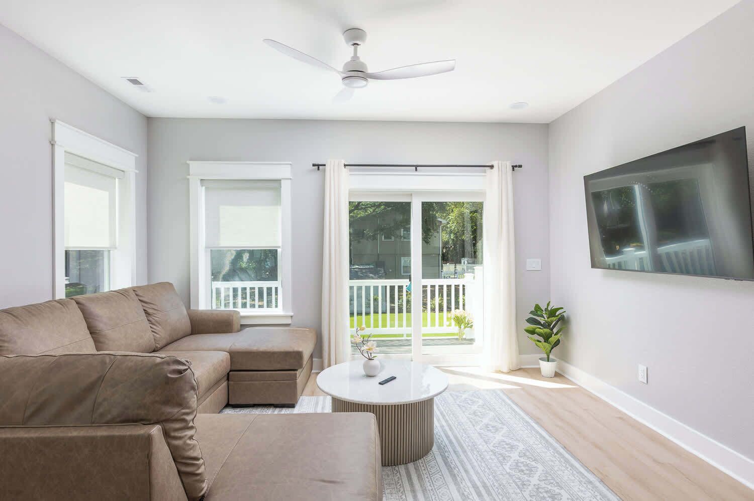 A modern living room with a sectional sofa, a round coffee table, and a flat-screen TV mounted on the wall.
