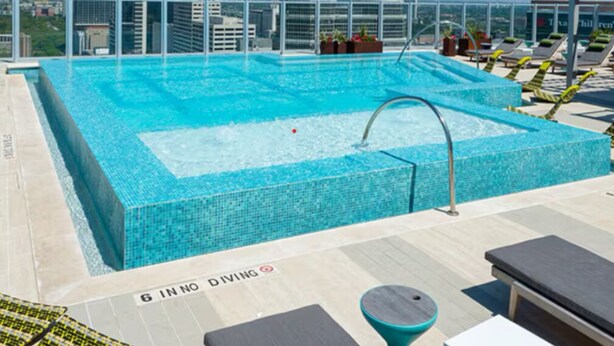 Ein Pool auf dem Dach mit Blick auf die Stadt, Liegestühle und ein Schild, das das Sprungverbot anzeigt.