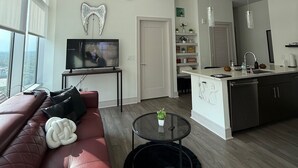 Ein modernes Wohnzimmer mit einem roten Sofa, einem Flachbildfernseher, einem Deckenventilator und Blick auf die Stadt durch große Fenster.