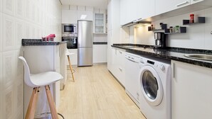A modern kitchen with white cabinets, a built-in oven, a microwave, a stainless steel refrigerator, a washing machine, and a coffee maker. - Apartment 'Osiris' with Wi-Fi (San Andrés del Rabanedo)