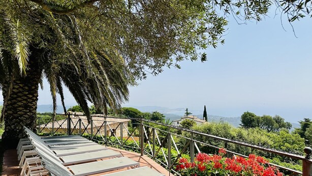 Eine Terrasse mit weißen Liegestühlen, Blick aufs Meer und roten Blüten.