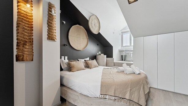 A modern bedroom with a curved bed, a wooden wall art piece, and a round woven wall hanging. - GuestReady - AMMA Braga - 8 (Braga)