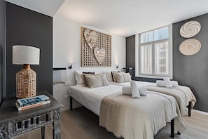 Een moderne slaapkamer met een groot bed, nachtkastjes, een wandlamp en een raam met gordijnen.