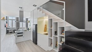A modern kitchen with a built-in stove, a refrigerator, and a staircase leading to a darkened upper level. - GuestReady - AMMA Braga - 8 (Braga)