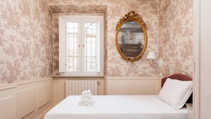 A neatly made bed with white linens and a folded towel, a gold-framed mirror, and a window with white shutters. - Candy Lodge - Three Bedroom Apartment, Sleeps 4 (Rome)