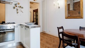 A kitchen with white cabinets, a stove, and a dining area with a wooden table and chairs. - Candy Lodge - Three Bedroom Apartment, Sleeps 4 (Rome)