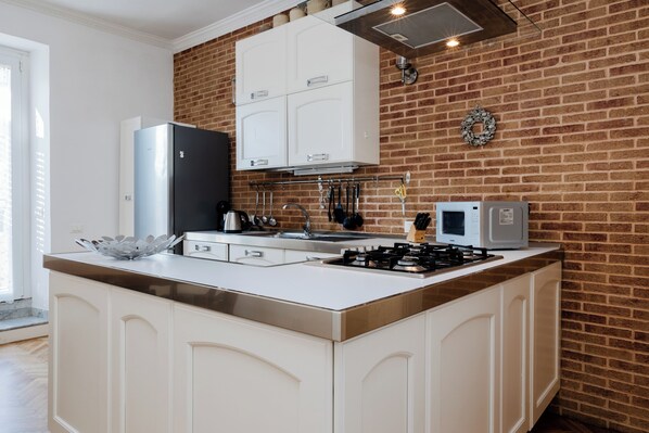 Una cocina con isla central, armarios blancos, pared de ladrillo y refrigerador de acero inoxidable.