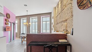 A modern dining area with a bench and table, a pink wall with decorative plates, and a stone wall with woven baskets. - GuestReady - AMMA Braga - 7 (Braga)