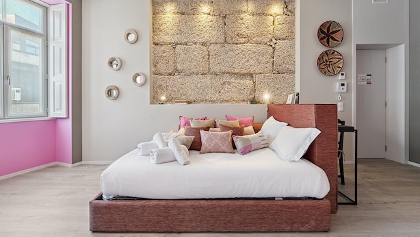 A modern bedroom with a stone wall headboard, a bed with multiple pillows, and a bedside table. - GuestReady - AMMA Braga - 7 (Braga)