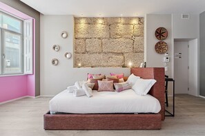A modern bedroom with a stone wall headboard, a bed with multiple pillows, and a bedside table. - GuestReady - AMMA Braga - 7 (Braga)