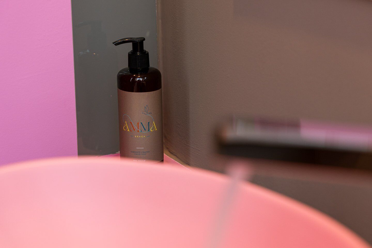 Une salle de bain avec un lavabo rose et un flacon de savon liquide portant l’étiquette « AMMA BRAGA ».