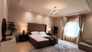 A modern hotel room with a large bed, bedside lamps, a sofa, and a chandelier.