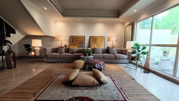 A modern living room with a large sofa, two side tables, and a coffee table. There are two lamps on the side tables and a large window providing natural light.