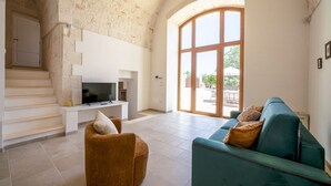 A living room with a TV, a sofa, a chair, and a staircase. - Palmento Giorgio: historic countryside retreat in the Itria Valley (Martina Franca)